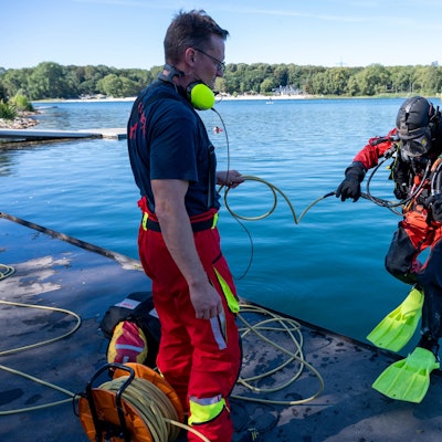 Ein Feuerwehrtaucher lässt sich rückwärts von einem Ponton ins Wasser fallen.