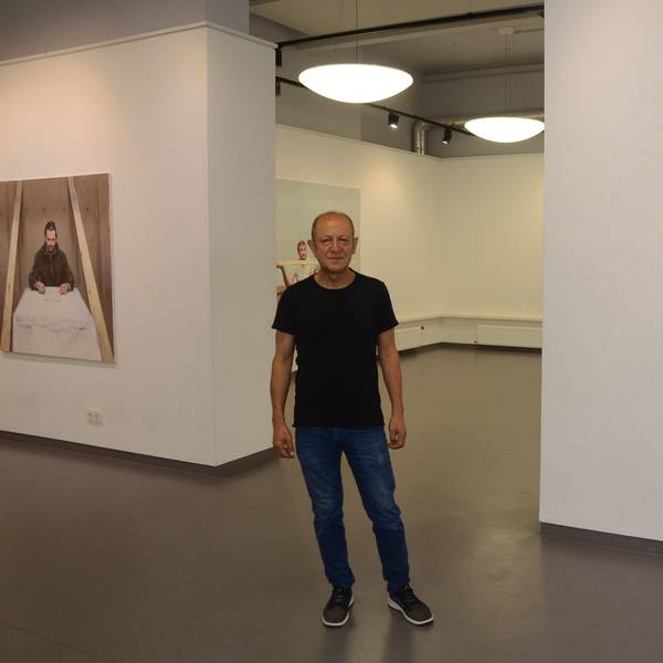 Ein Mann im schwarzen T-Shirt, Jeans und dunklen Sneakern steht im Ausstellungsraum. Links und rechts hängen Bilder, die er gemalt hat.