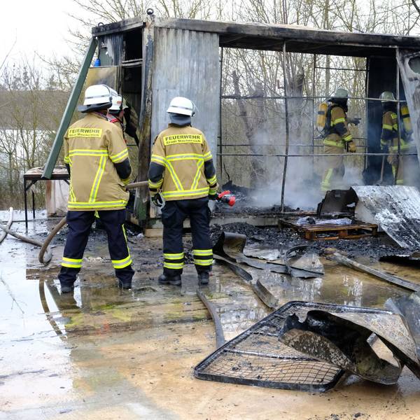 Feuerwehrleute stehen in Mechernich vor und in einem Wohncontainer, der durch einen Brand völlig zerstört worden ist.