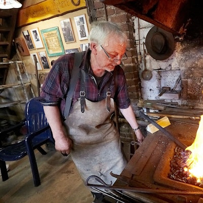 Der Schmied Stefan Pütz steht in einer alten Werkstatt an einem Kohlenfeuer.