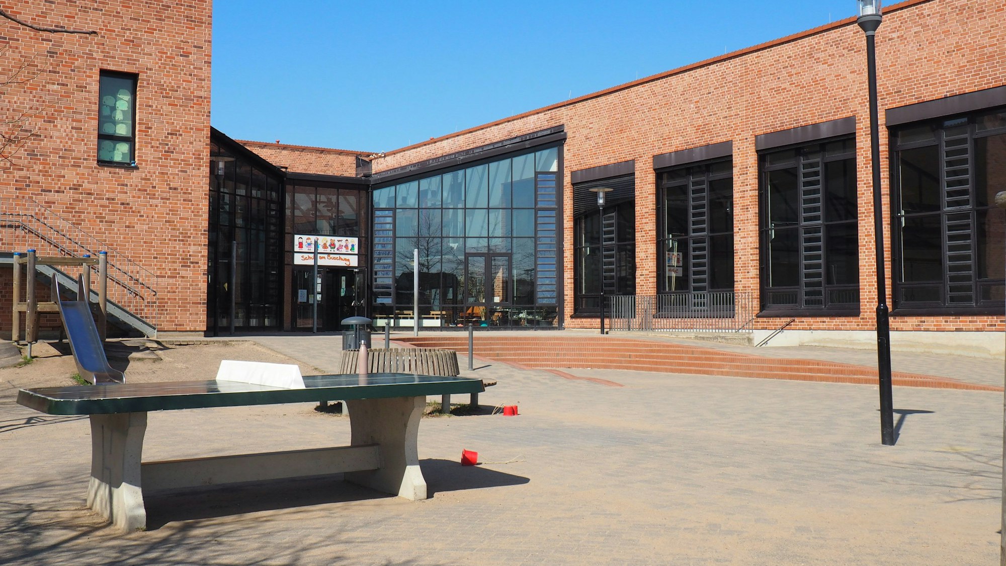 Vor einem Schulgebäude aus Backstein steht eine Tischtennisplatte.