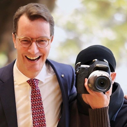 Auf einem gefälschten Bild ist Ministerpräsident Wüst zu sehen, wie er lachend einem Fotografen den Arm um die Schulter legt. Dessen Gesicht ist hinter einer Kamera verborge.