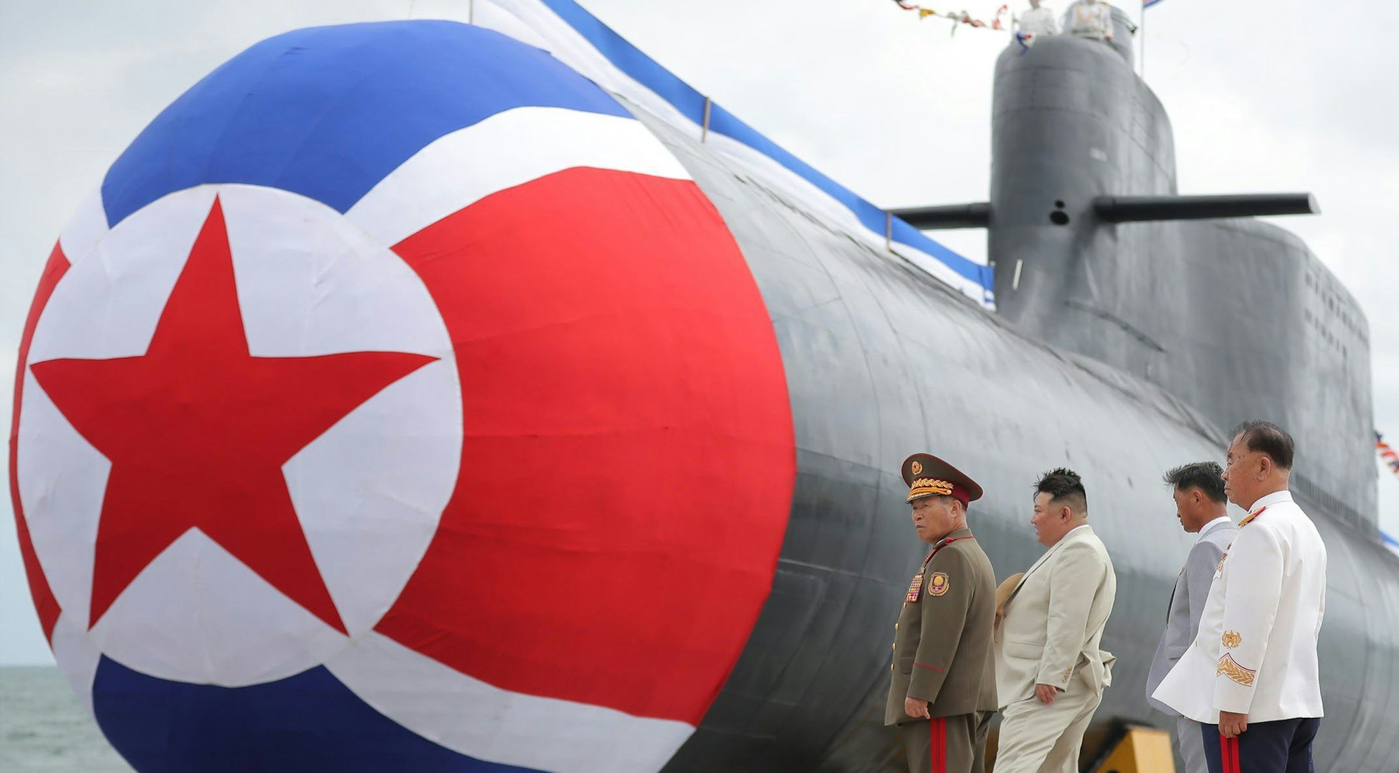 Der nordkoreanische Machthaber Kim Jong-un betrachtet mit einer Delegation ein neuartiges Atom-U-Boot. An der Front ist ein Teil der nordkoreanischen Flagge mit einem roten Stern zu sehen.