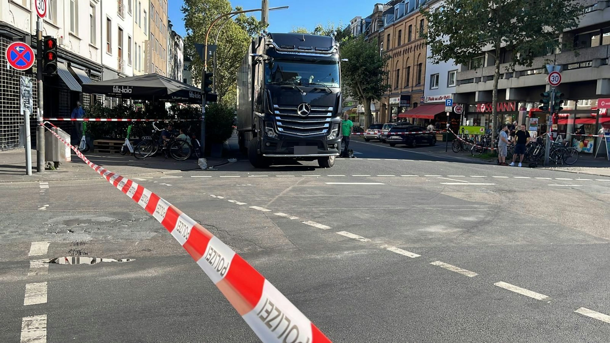 Ein Flatterband sperrt eine Straßenkreuzung ab, im Hintergrund steht ein dunkler Lkw am Straßenrand.