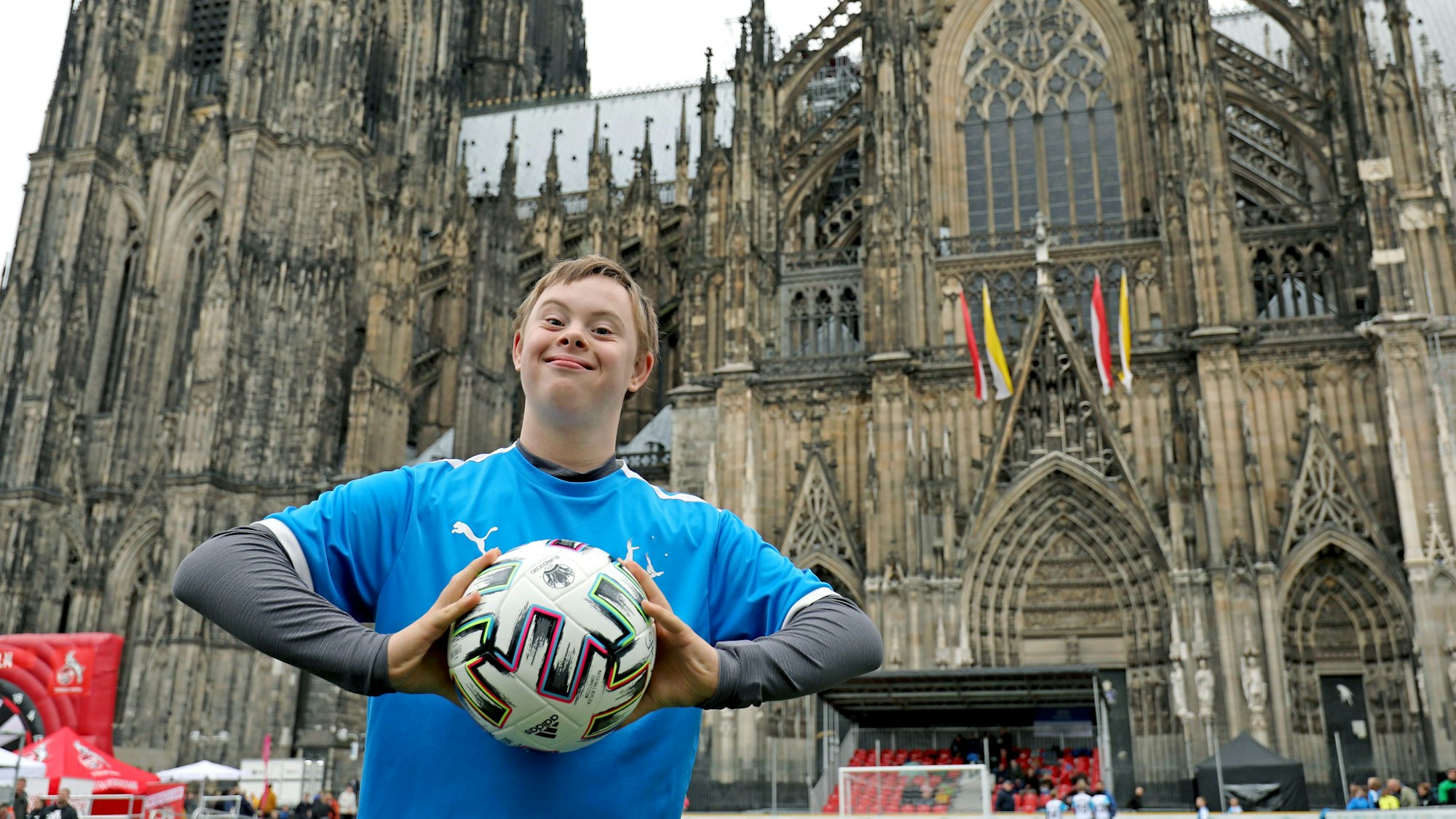 Ein Junge steht mit einem Fußball in der Hand vor dem Kölner Dom