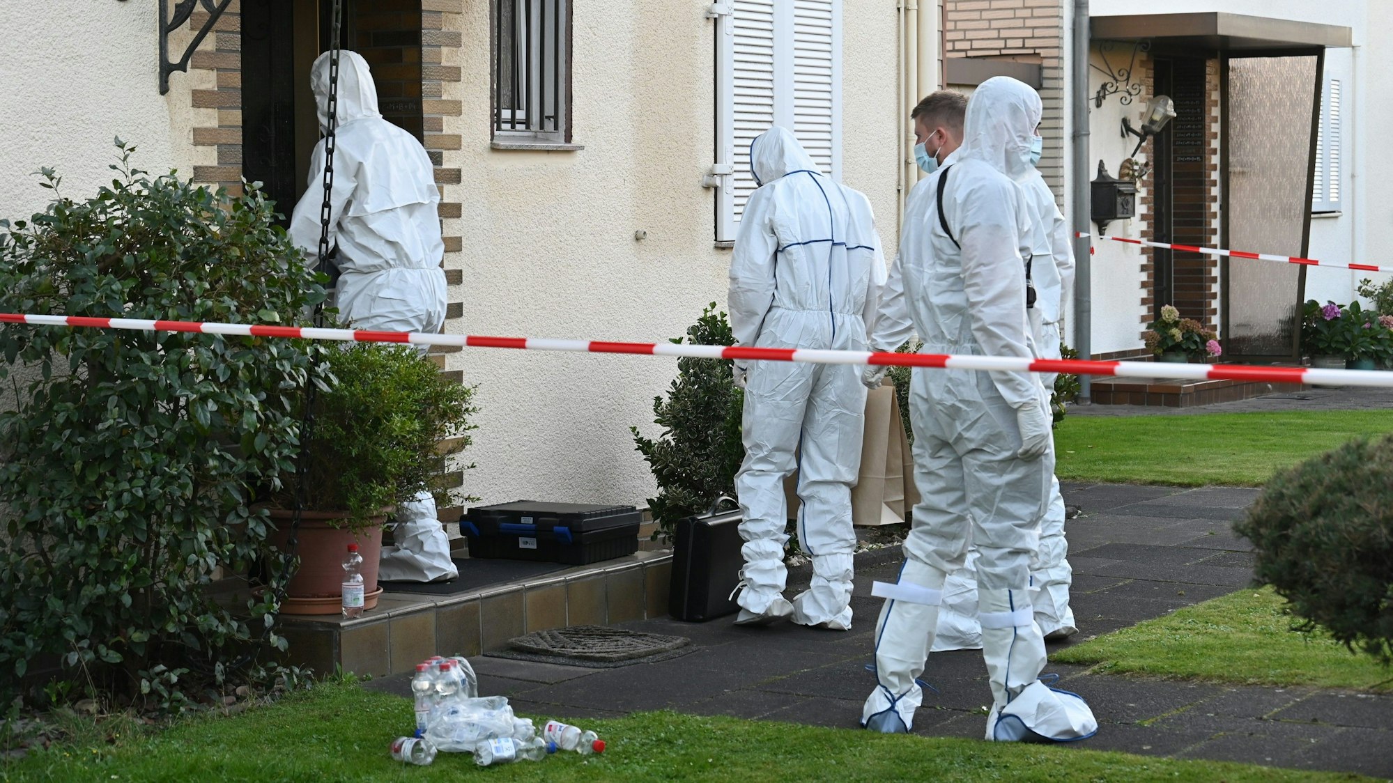 Auf dem Bild sind Ermittlungsbeamte in weißen Schutzanzügen vor dem Haus des Opfers zu sehen.