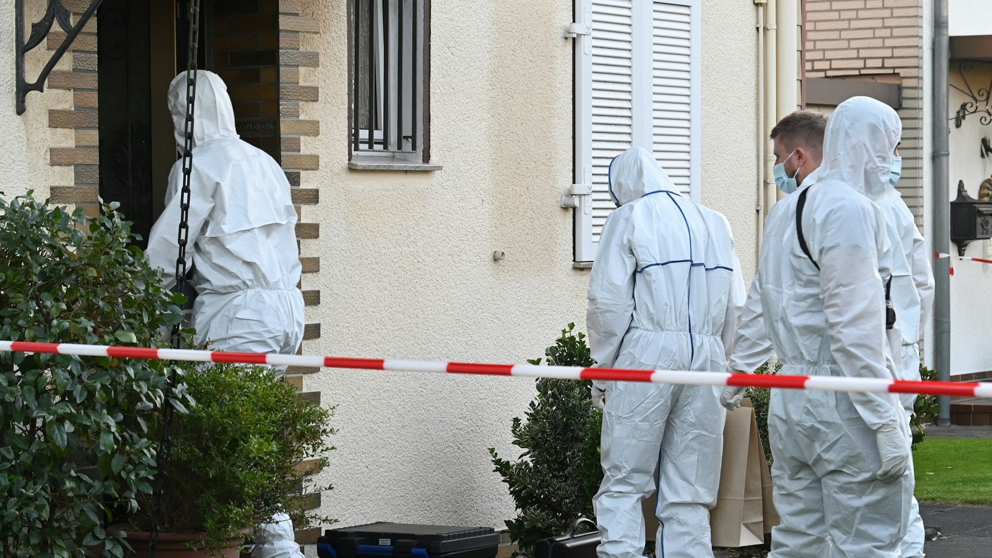 Das Foto zeigt Polizeibeamte in weißen Schutzanzügen vor dem Haus in Pulheim, die am Tatort Spuren gesichert haben.