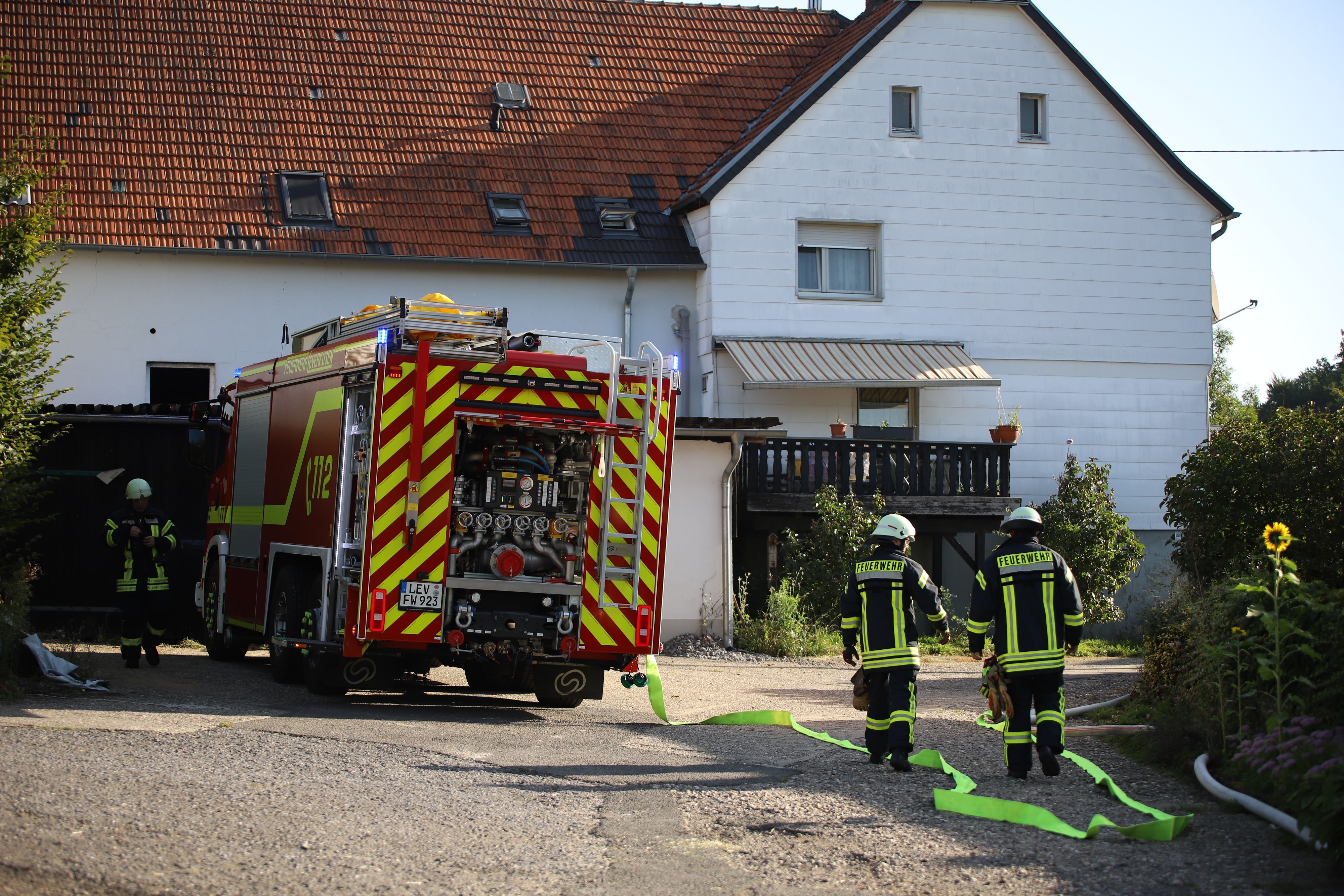 Es ist ein Haus zu sehen. Davor steht ein Wagen der Feuerwehr und zwei Einsatzkräfte.