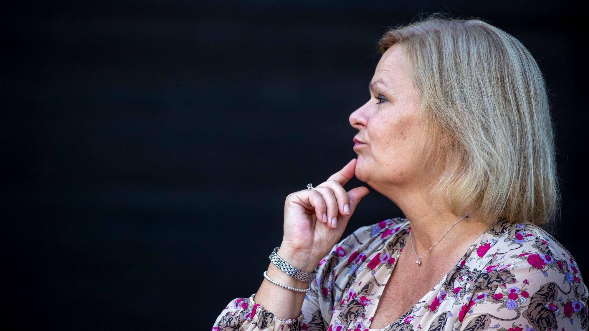 Die Bundesinnenministerin, Nancy Faeser, hält ihren Zeigefinger nachdenklich an ihr Kinn und schaut in die Ferne - der Hintergrund ist schwarz.