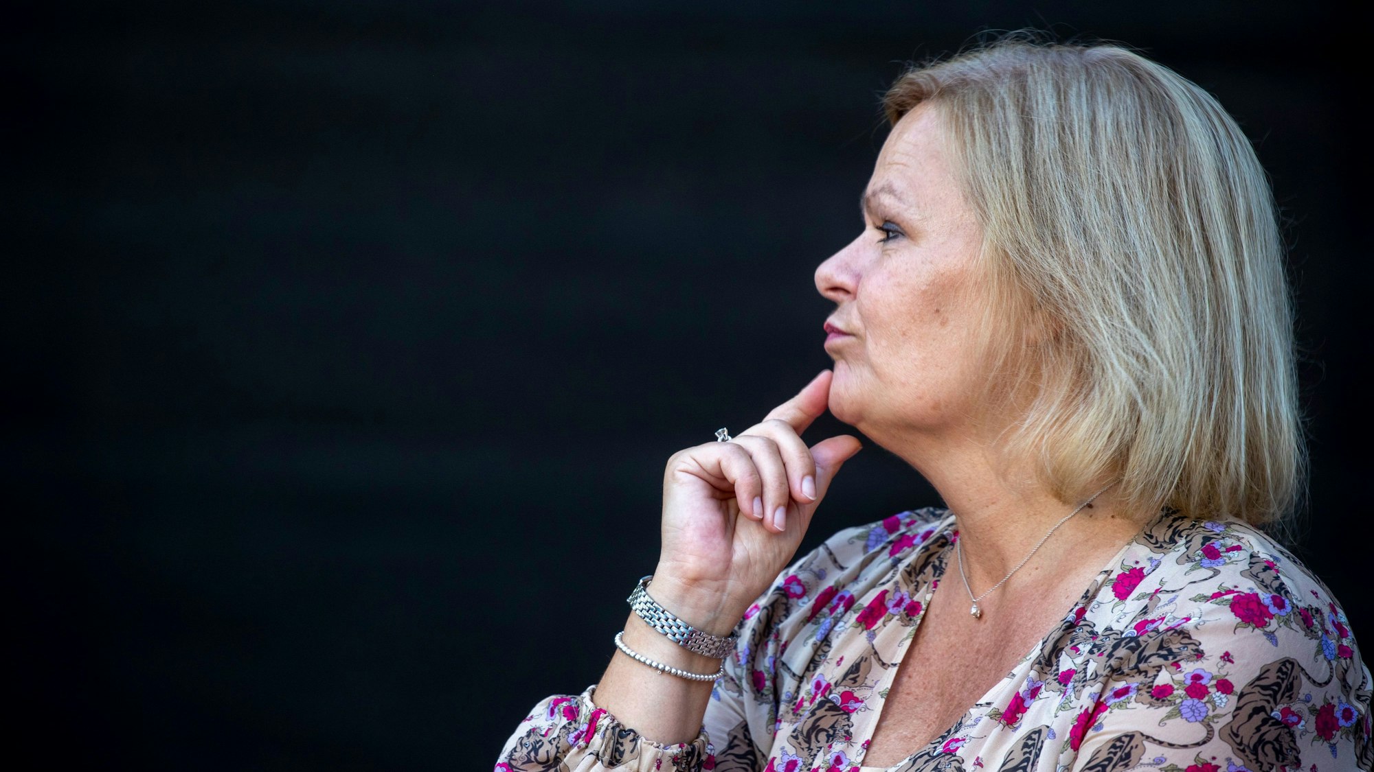 Die Bundesinnenministerin, Nancy Faeser, hält ihren Zeigefinger nachdenklich an ihr Kinn und schaut in die Ferne - der Hintergrund ist schwarz.