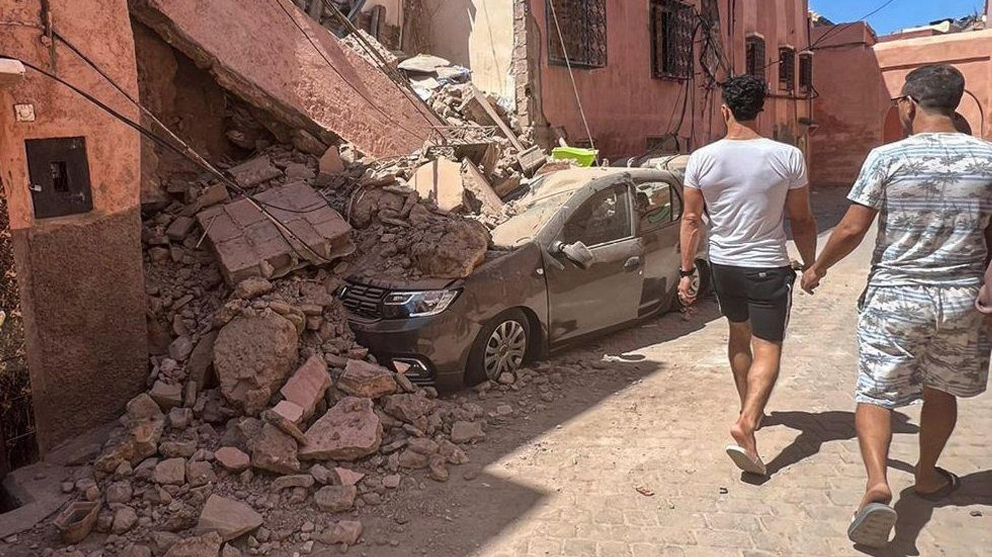 Erdbeben in Marokko: Zwei Männer gehen an einem eingestürzten Haus vorbei, die Trümmer haben ein Auto begraben.
