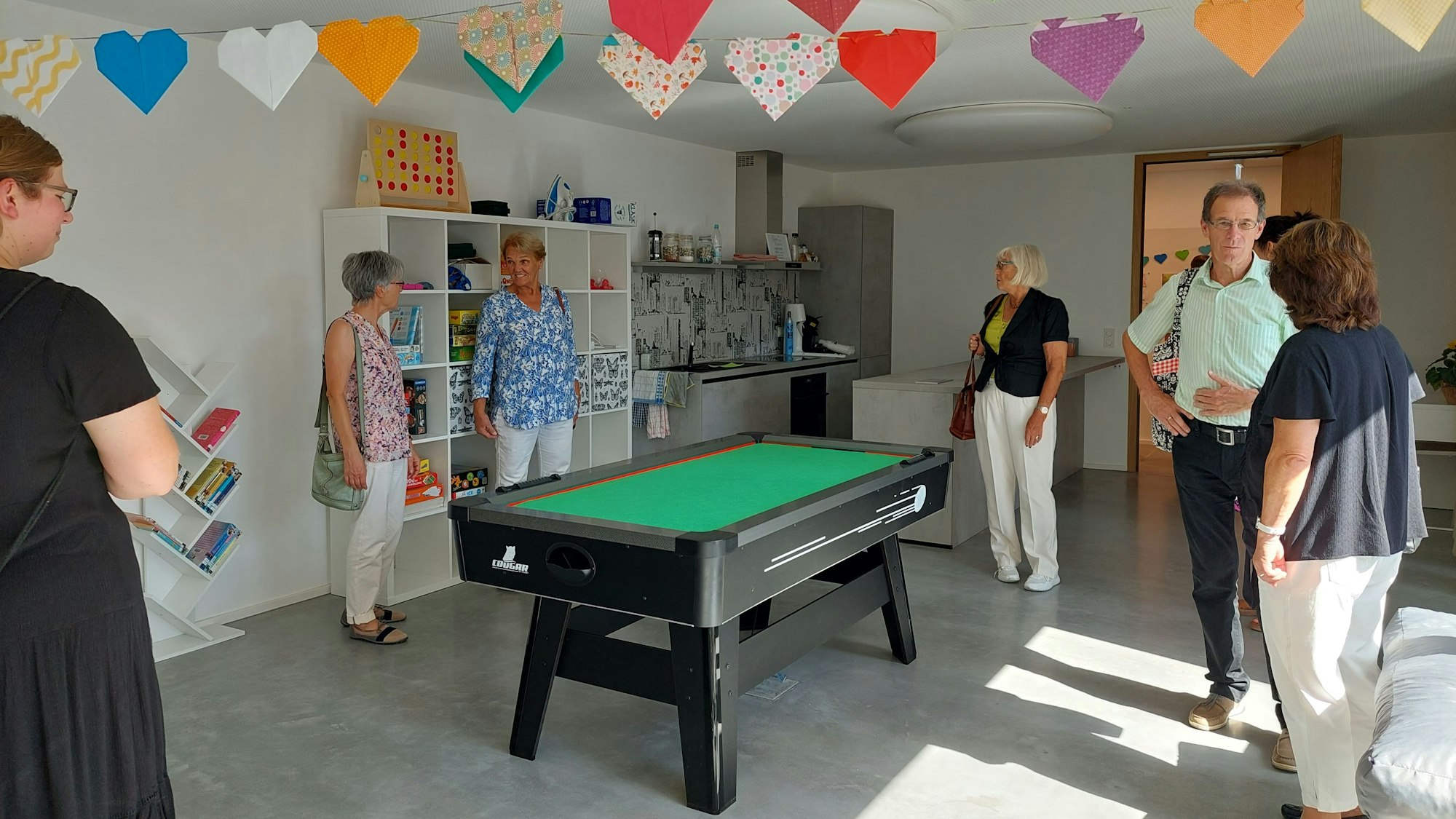 Raum mit Billardtisch und Menschen drumherum.