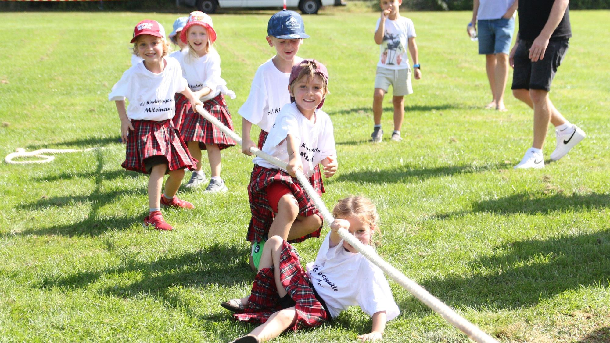 Kinder in Kilts und weißen T-Shirts ziehen an einem Tau.