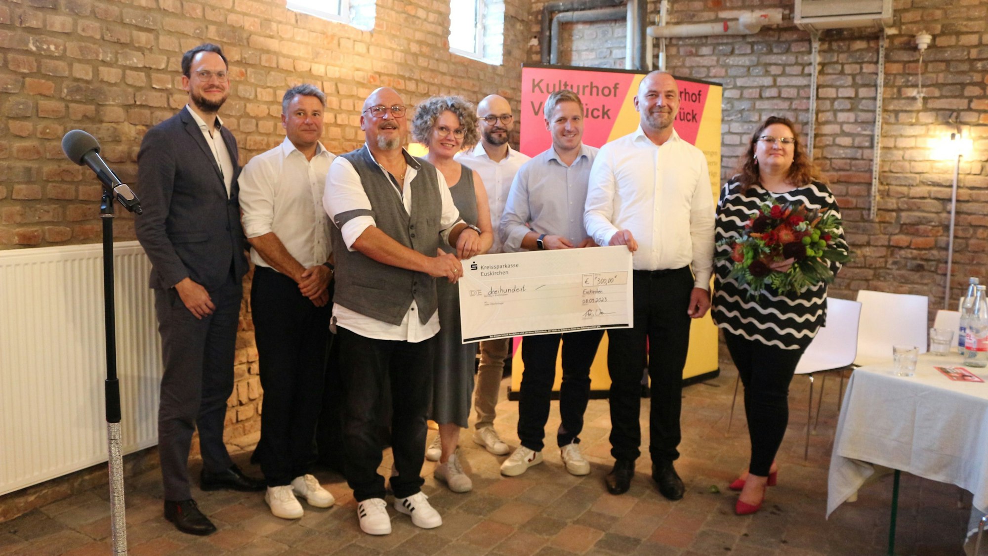 Eine Gruppe steht in einem Saal zusammen. Zwei Männer halten einen Scheck. Sie sind von der SPD im Kreis Euskirchen für ihr ehrenamtliches Engagement geehrt worden.