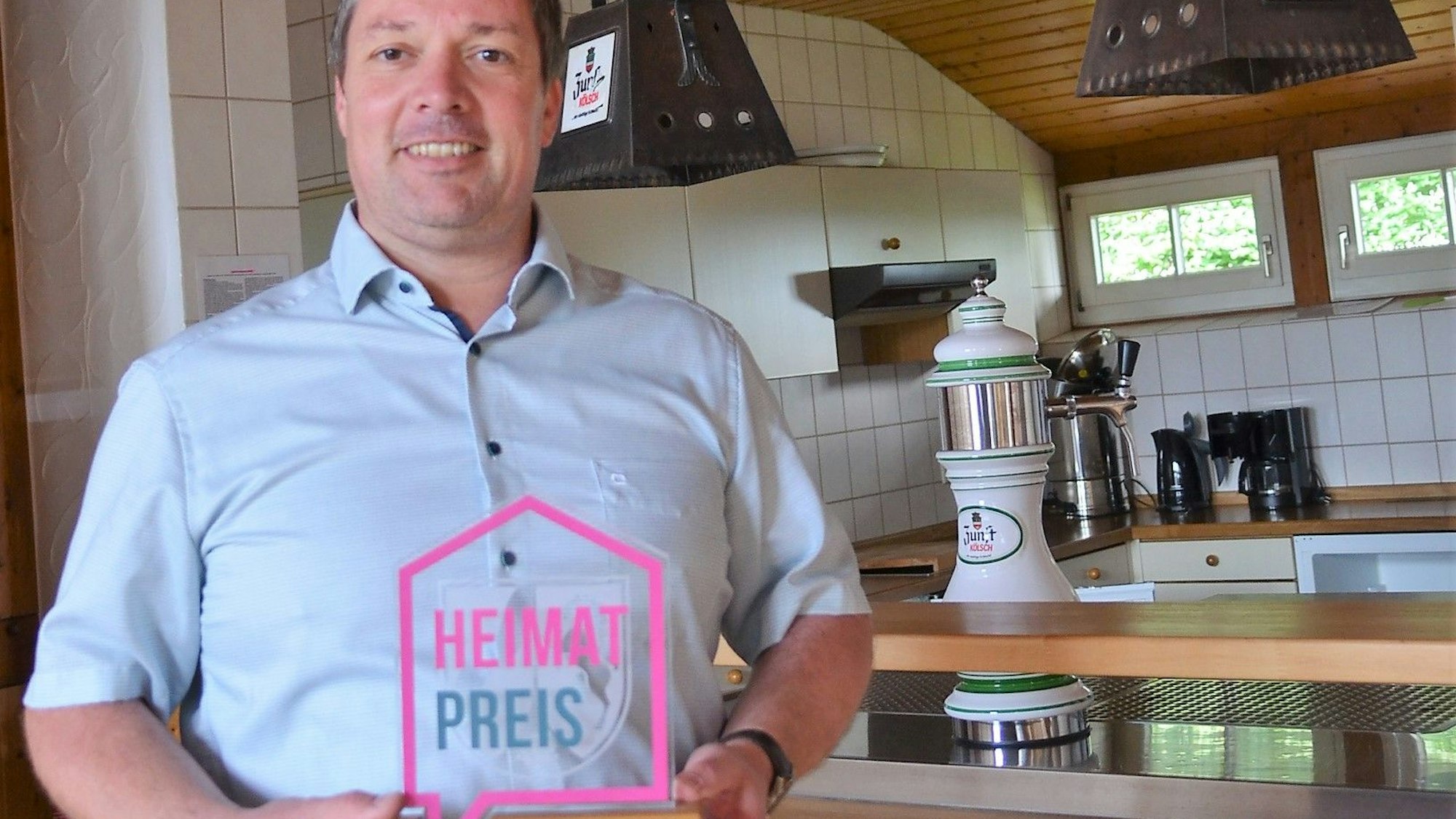 Stolz präsentiert Jan Wirths, Vorsitzender des Trägervereins „Alter Schulbezirk Wallerhausen“, den Heimat-Preis, den sein Verein 2021 für ein erstes Projekt am Dörfergemeinschaftshaus in Morsbach-Wallerhausen erhalten hat. Wirths steht in dem Saal, der künftig auch vermietet werden soll.