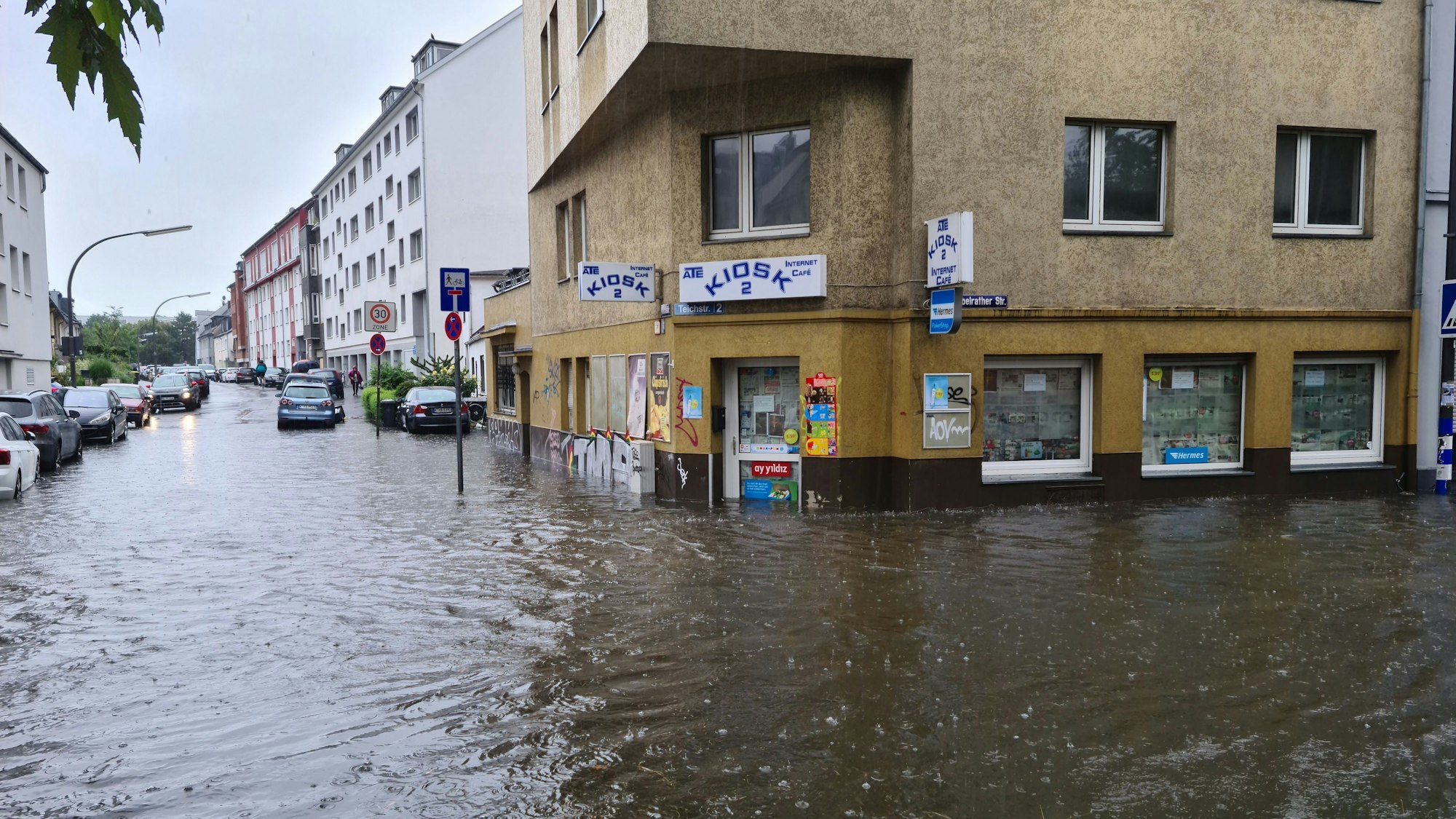 Eine Straßenkreuzung ist überflutet, Häuser stehen bis zur Fensterunterkante im Wasser.