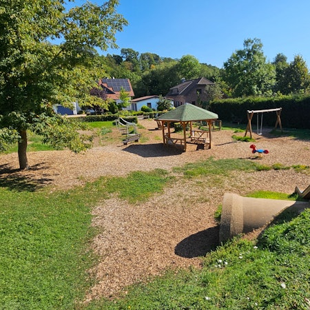Zu sehen ist ein Spielplatz, auf dessen Fläche Holzhackschnitzel verteilt wurden.