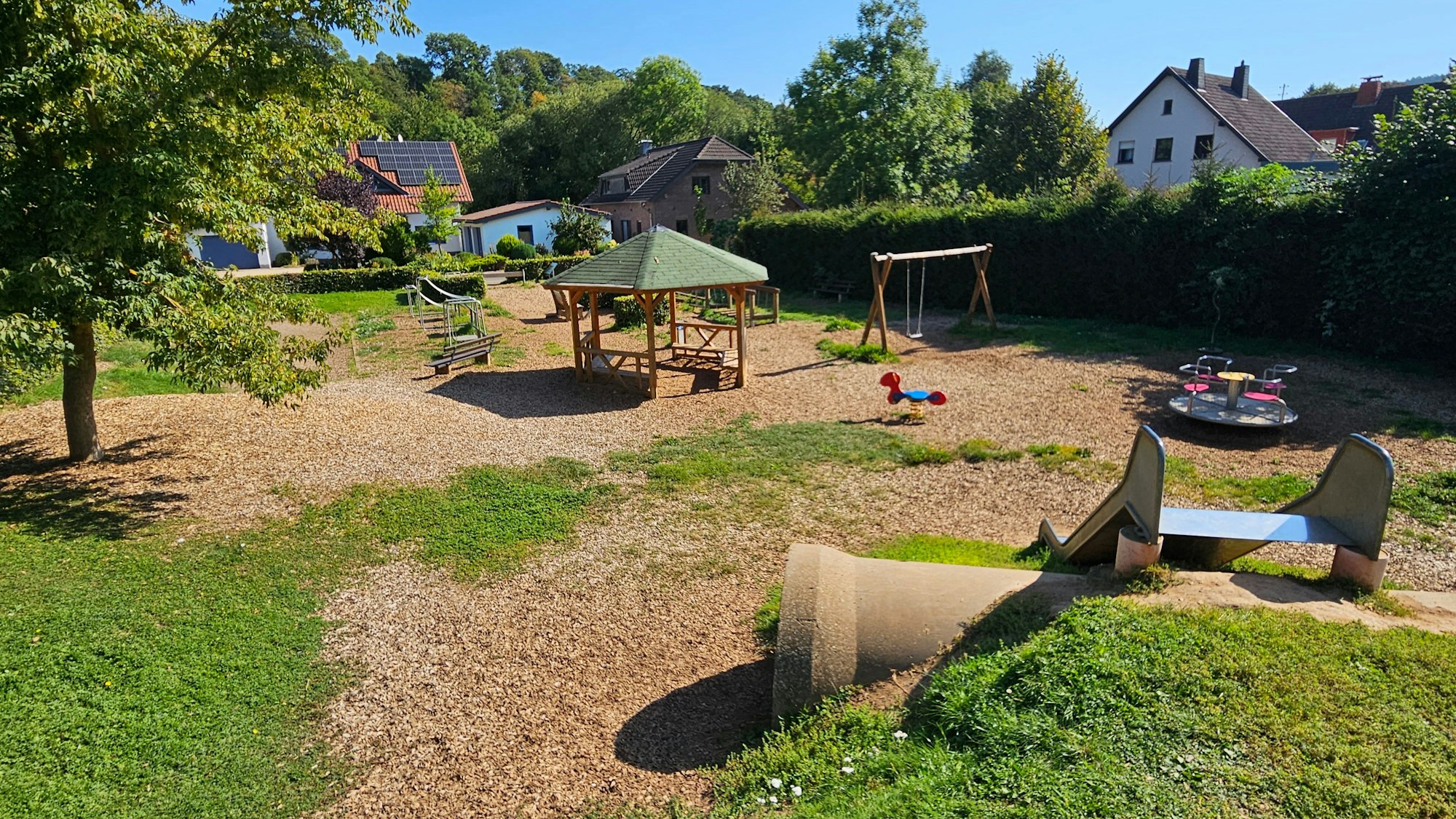 Zu sehen ist ein Spielplatz, auf dessen Fläche Holzhackschnitzel verteilt wurden.