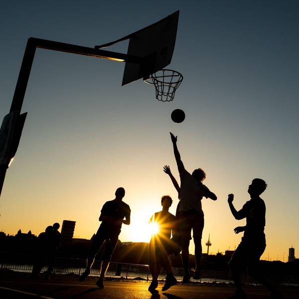 Männer spielen im Licht der untergehenden Abendsonne Basketball am Rheinufer.
