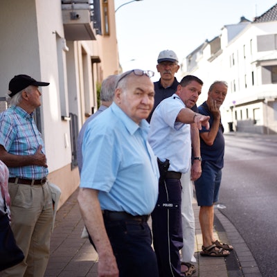 Ein Polizist steht mit Senioren und Seniorinnen in Euskirchen am Straßenrand und erklärt ihnen das richtige Verhalten im Straßenverkehr.