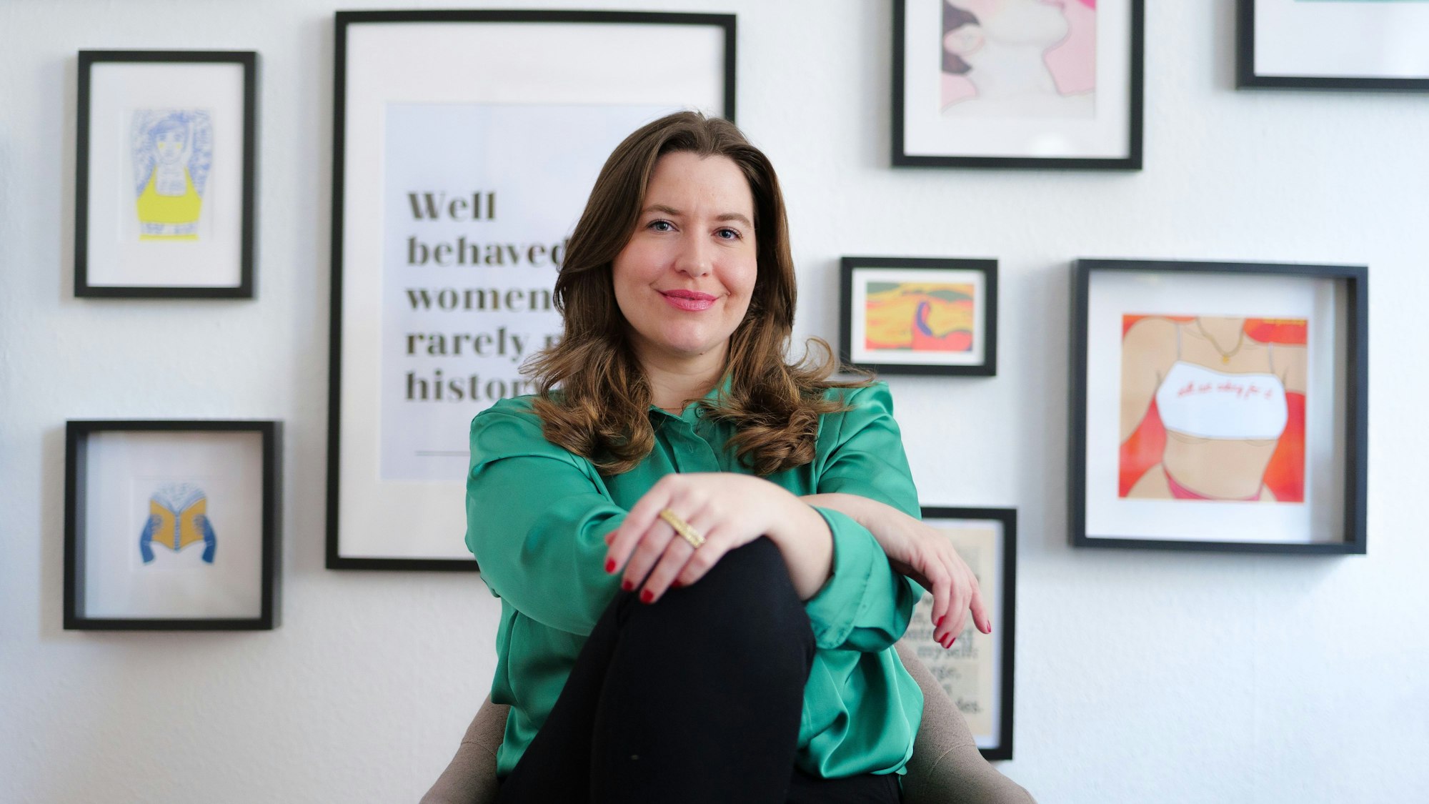 Madita Oeming sitzt vor einer Wand mit Bildern.