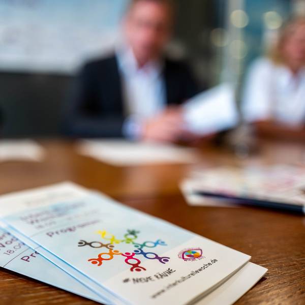 Das Bild zeigt den Flyer der Interkulturellen Wochen im Kreis Euskirchen. Im Hintergrund sind drei Menschen zu erahnen.