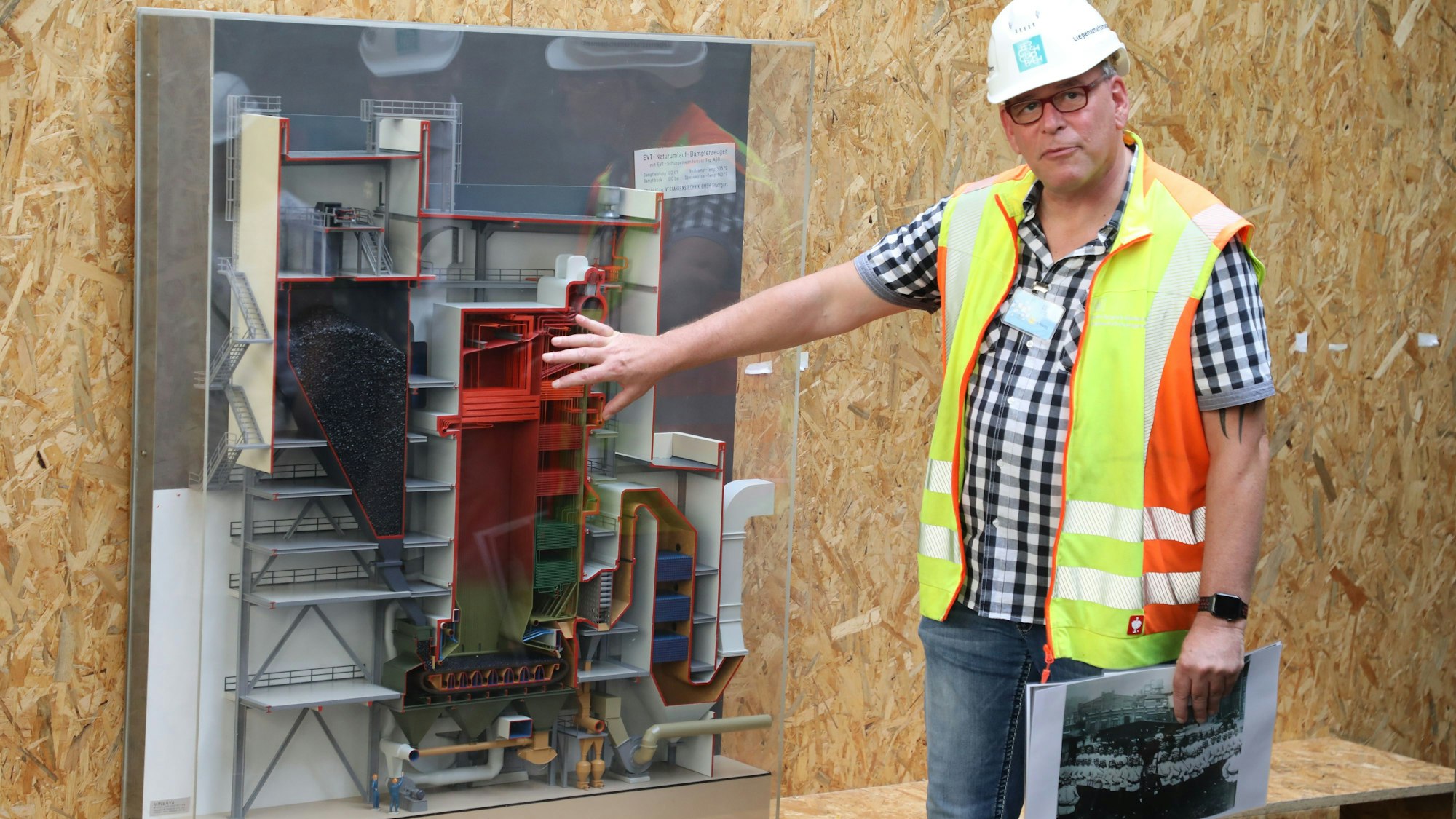 Ein Mann mit Helm und gelber Weste zeigt die Funktionsweise des Zanders-Kraftwerks anhand eines Modells.