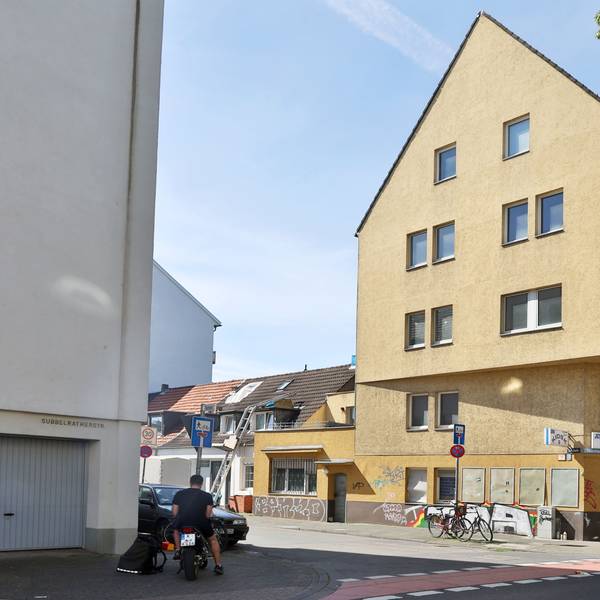 Ein sehr großes Eckhaus mit gelbem Anstrich und Ladenlokal im Erdgeschoss ist zu sehen.