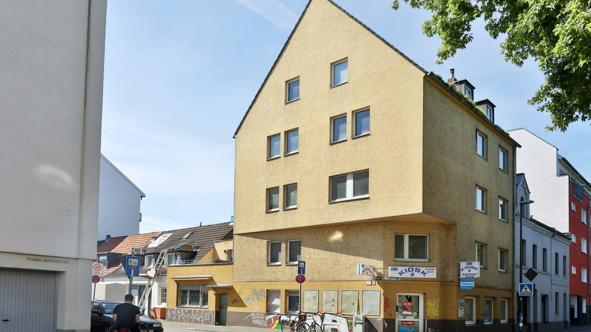 Ein sehr großes Eckhaus mit gelbem Anstrich und Ladenlokal im Erdgeschoss ist zu sehen.