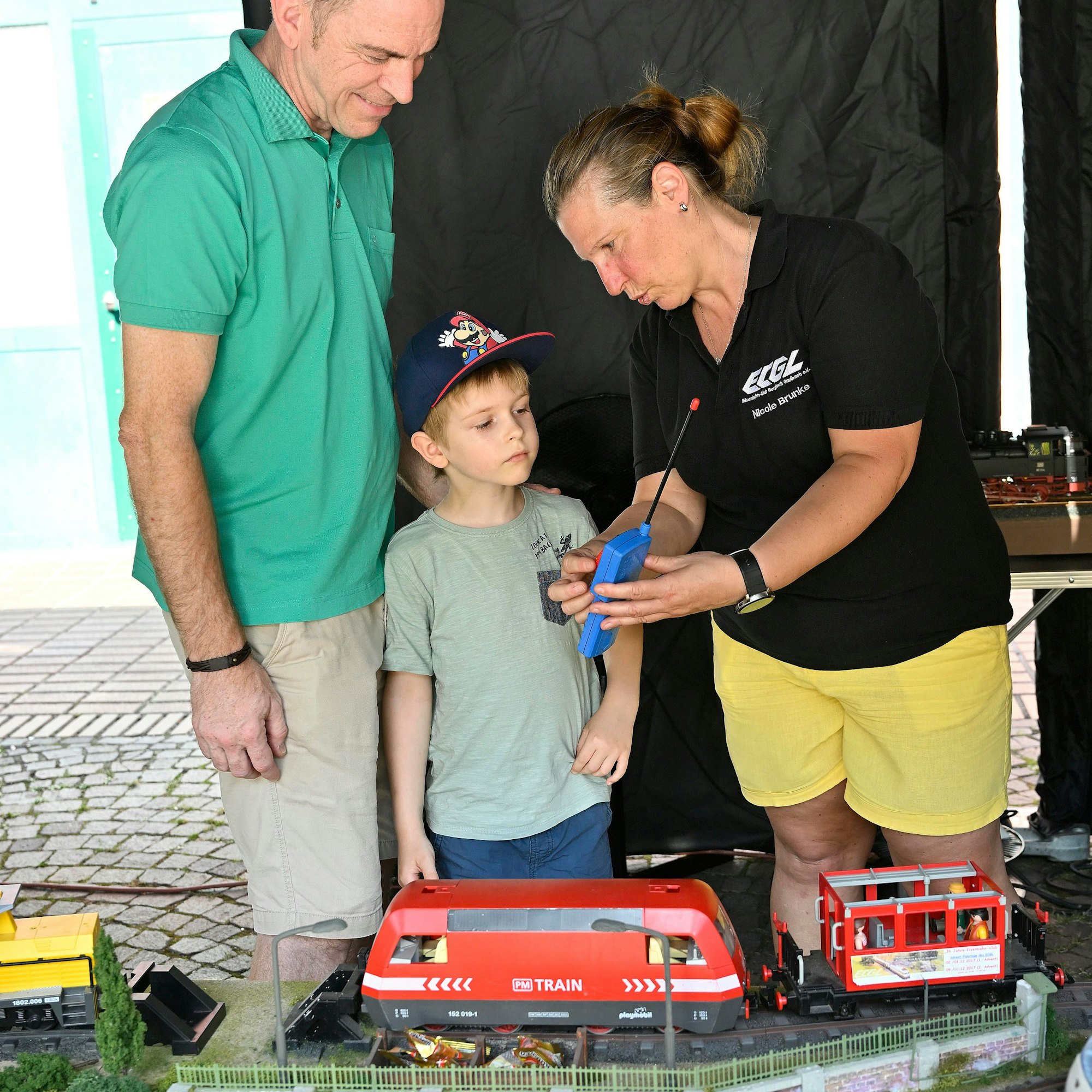 Einen Frau erklärt einem Kind und einem Mann die Fernbedienung einer Modellbahn.