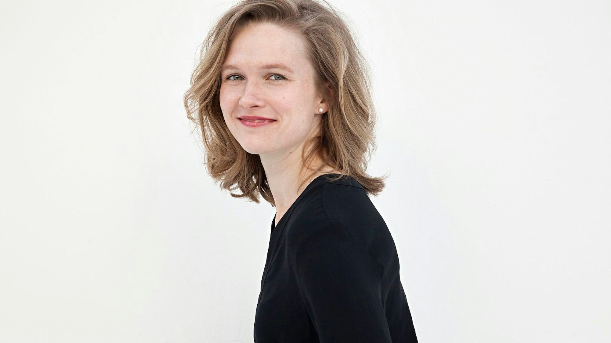 Mirga Gražinytė-Tyla ist blond und trägt einen schwarzen Pulli. Sie steht seitlich zur Kamera und lächelt ihr zu.