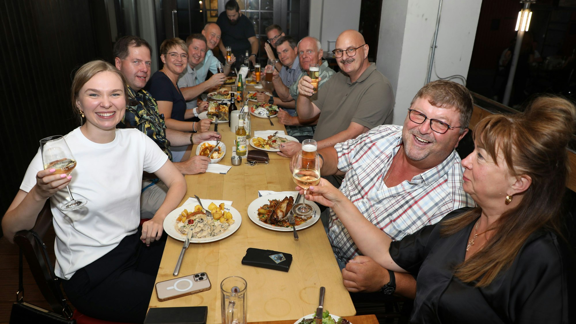 Menschen sitzen um einen Tisch und prosten sich zu.