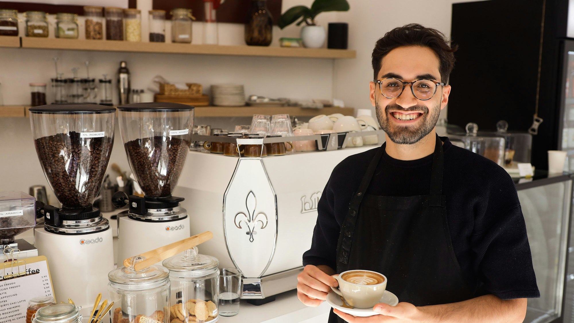 Ibrahim Isiksoy steht mit einer Tasse Cappuccino in seinem Cafe Goldzeit.