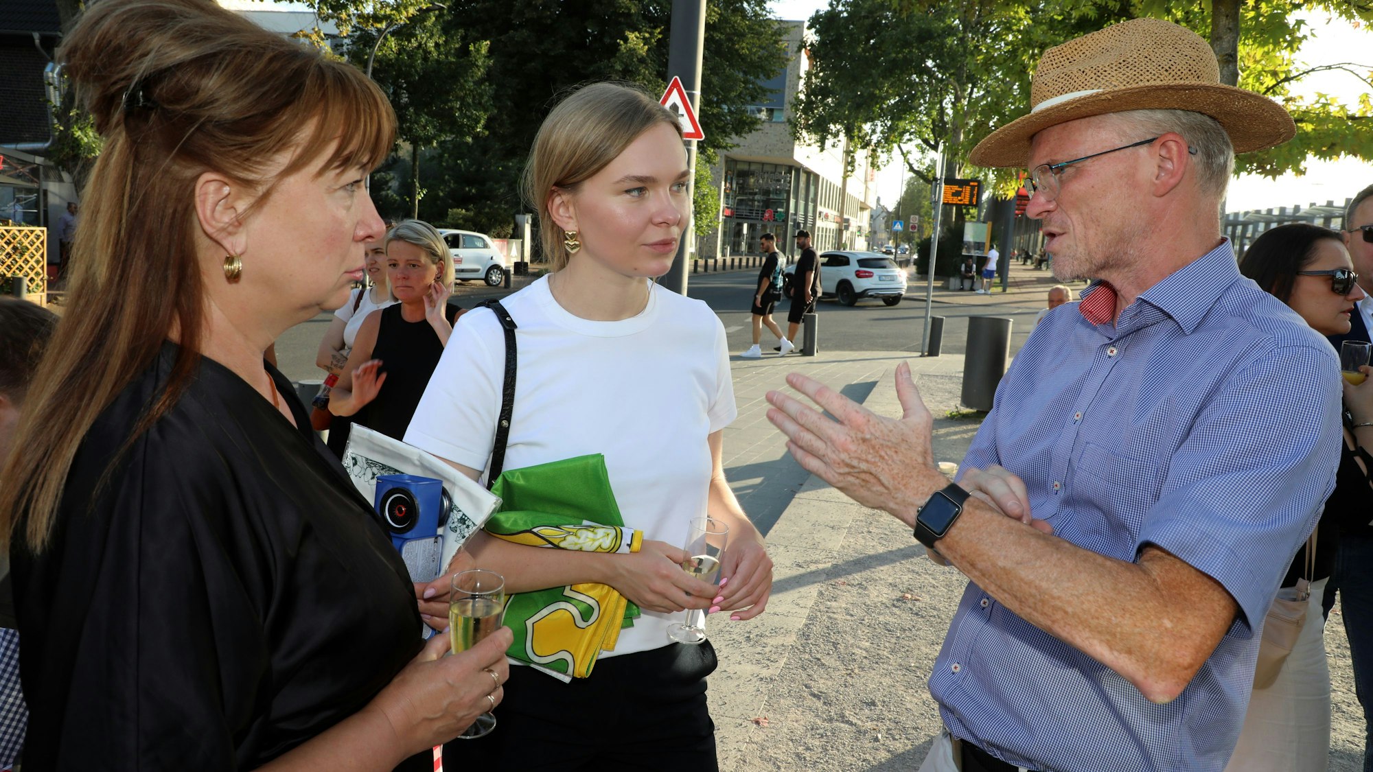 Zwei Frauen und ein Mann stehen auf einem Platz und sprechen miteinander.