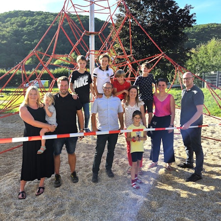 Eine Gruppe aus Kindern und Erwachsenen steht an und auf einer Kletterpyramide aus roten Seilen.