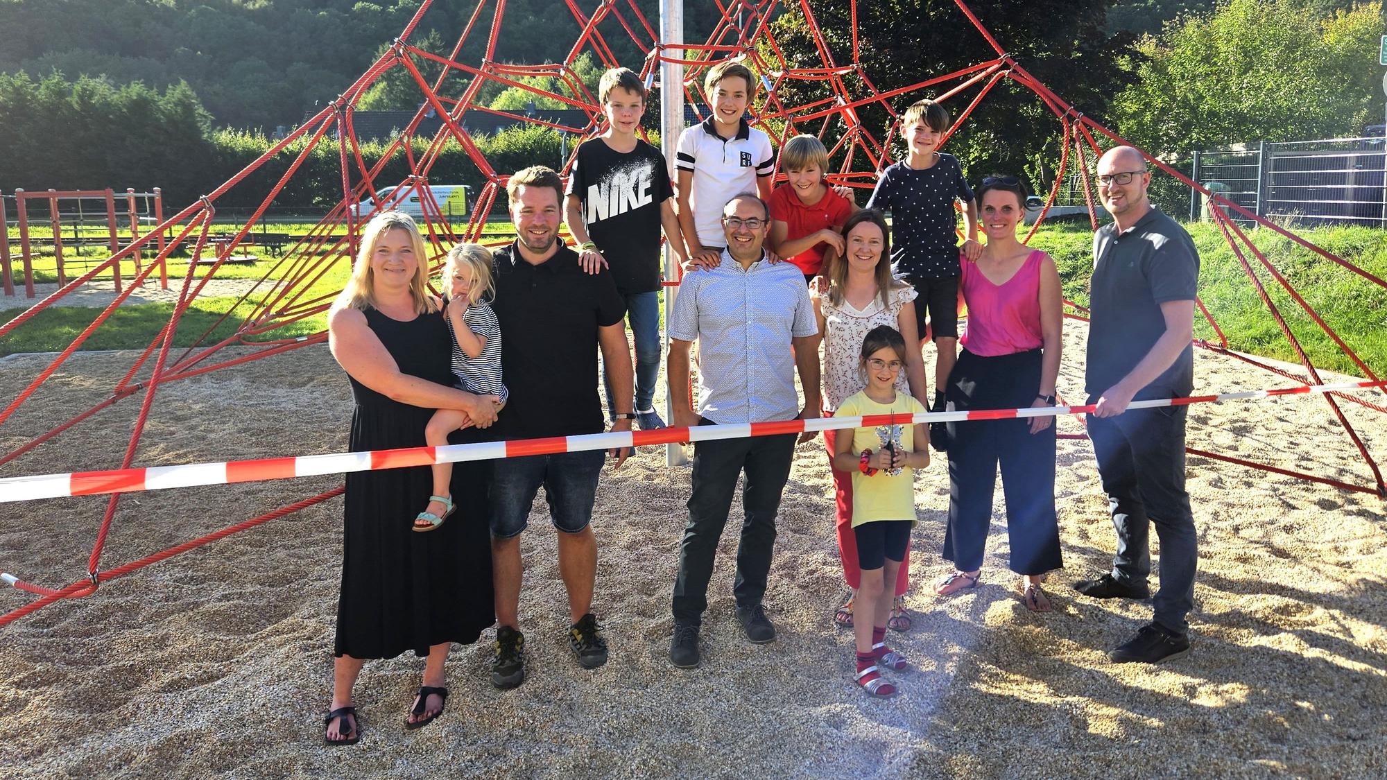 Eine Gruppe aus Kindern und Erwachsenen steht an und auf einer Kletterpyramide aus roten Seilen.