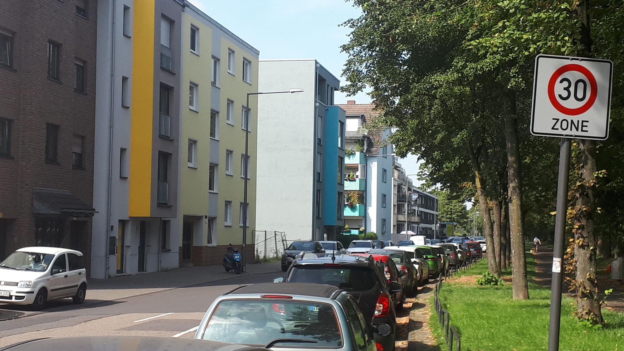 EinTempo-30-Schild steht am Rande einer Straße, auf der viele Autos parken.