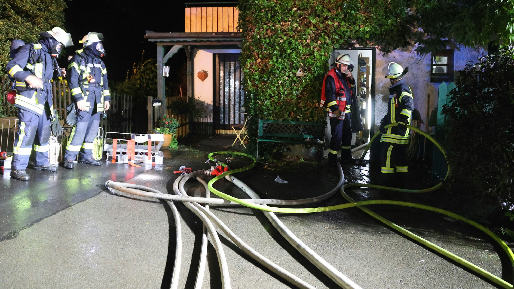 Vor einem nächtlich erleuchteten Haus sind Feuerwehrleute und Schläuche zu sehen.