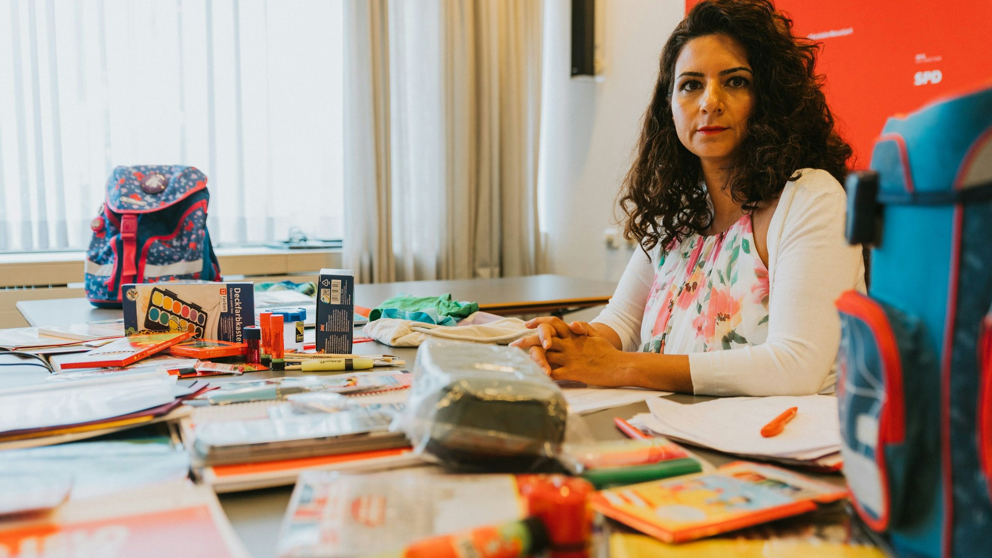 Dilek Engin sitzt an einem Schreibtisch inmitten von Schulmaterial, das für den Schulbeginn angeschafft wurde.