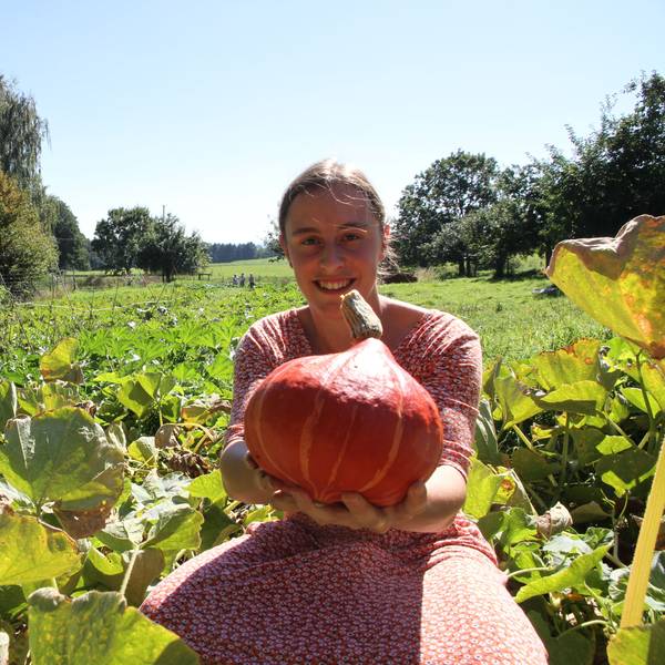 Pauline Gödecke von der solidarischen Landwirtschaft in Much hält auf einem Feld einen orangefarbenen Kürbis in die Kamera