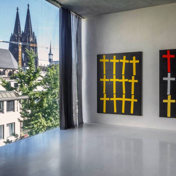 Zwei Bilder mit Kreuzen hängen neben einem Fenster, durch das der Kölner Dom zu sehen ist.