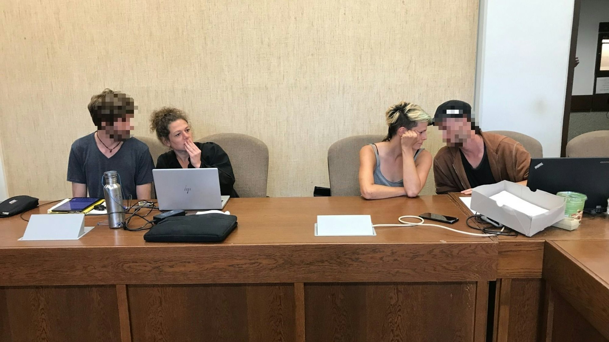 Vier Personen sitzen in einem Gerichtssaal.