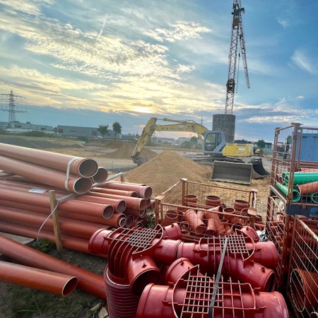 Zu sehen ist eine Baustelle mit einem Kran und roten Rohren.