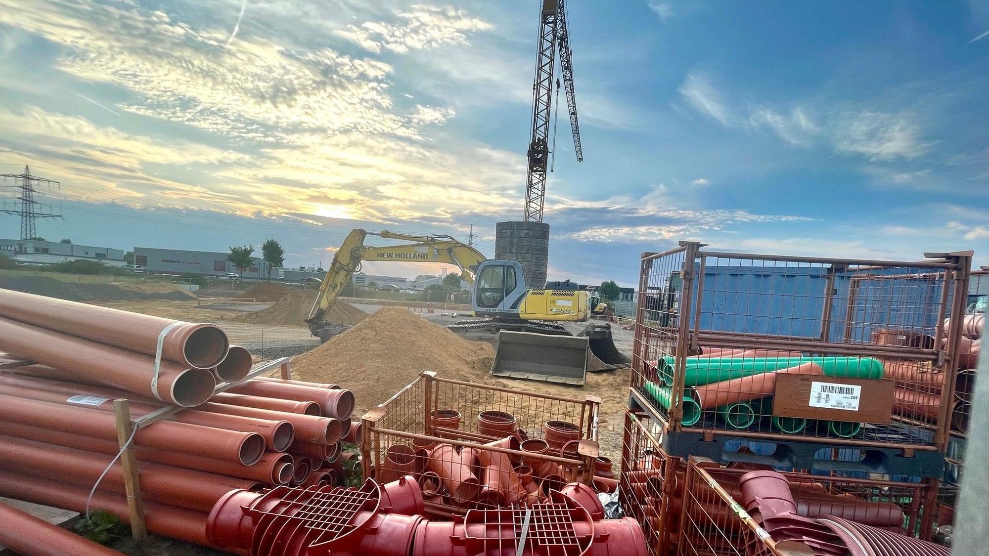 Zu sehen ist eine Baustelle mit einem Kran und roten Rohren.