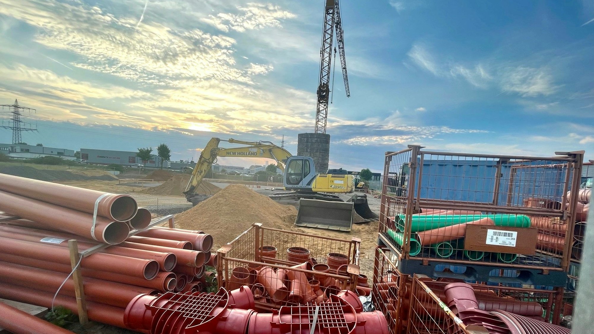Zu sehen ist eine Baustelle mit einem Kran und roten Rohren.
