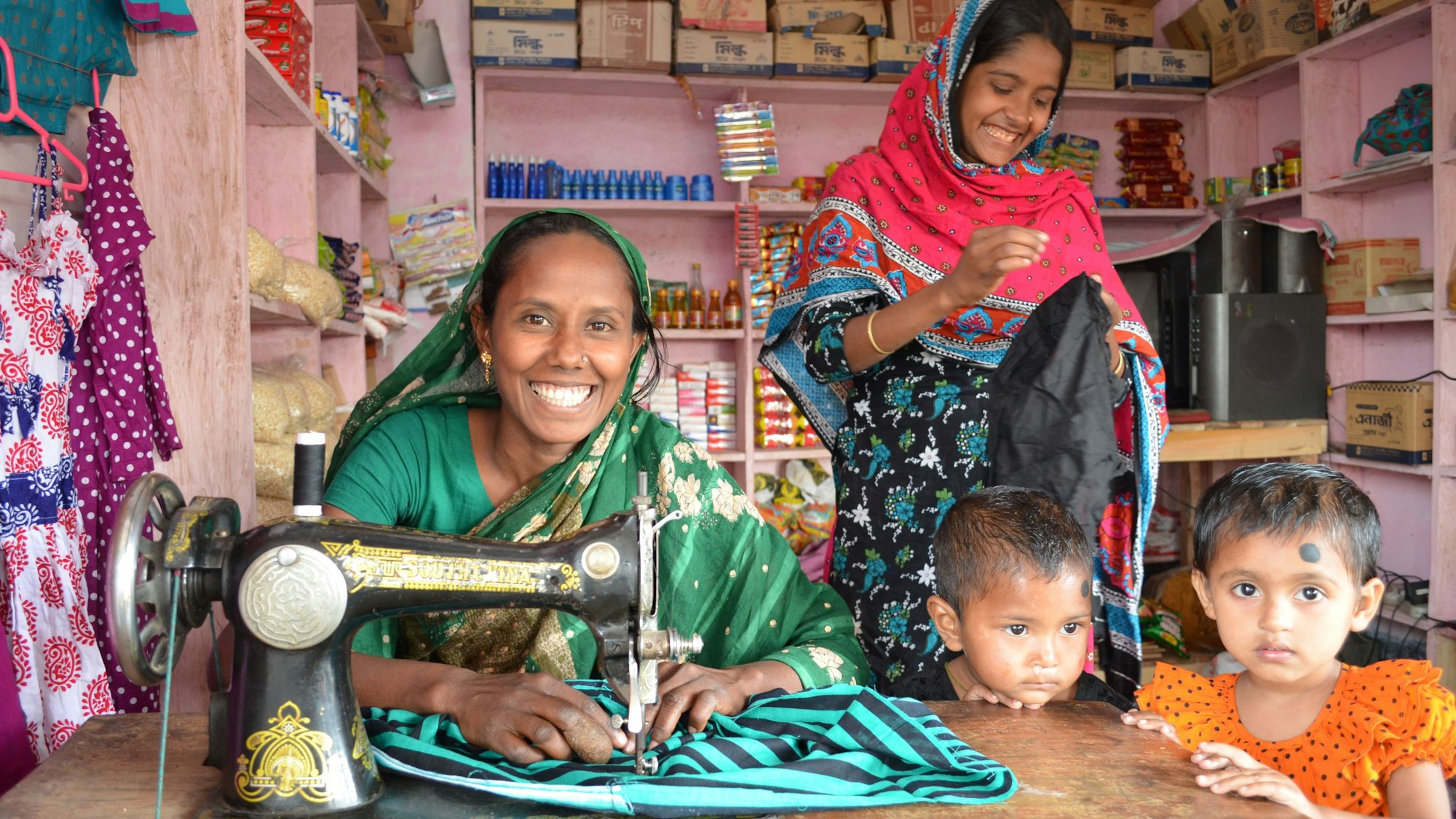 Eine junge Frau sitzt an einer Nähmaschine. Neben ihr stehen zwei Kinder.