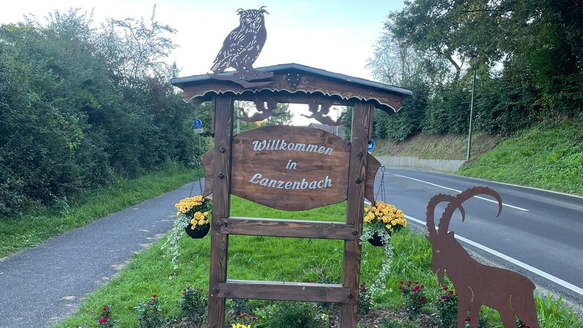 Das Willkommensschild mit dem Schriftzug „Willkommen in Lanzenbach“ steht auf einem Grünstreifen neben der Straße.