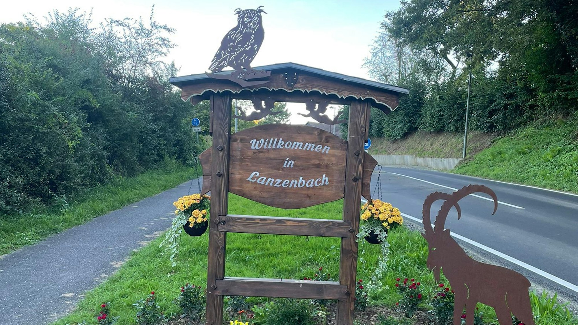 Das Willkommensschild mit dem Schriftzug „Willkommen in Lanzenbach“ steht auf einem Grünstreifen neben der Straße.