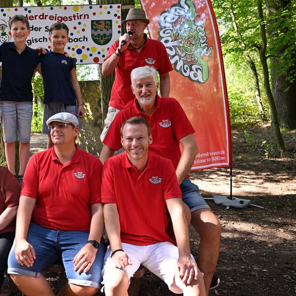 Das angehende Kinderdreigestirn der Kreisstadt Bergisch Gladbach steht im Wald vor einem Schild mit der Aufschrift „Kinderdreigestirn der Stadt Bergisch Gladbach“.