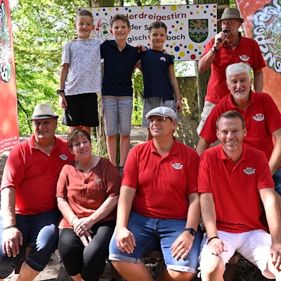 Das angehende Kinderdreigestirn der Kreisstadt Bergisch Gladbach steht im Wald vor einem Schild mit der Aufschrift „Kinderdreigestirn der Stadt Bergisch Gladbach“.